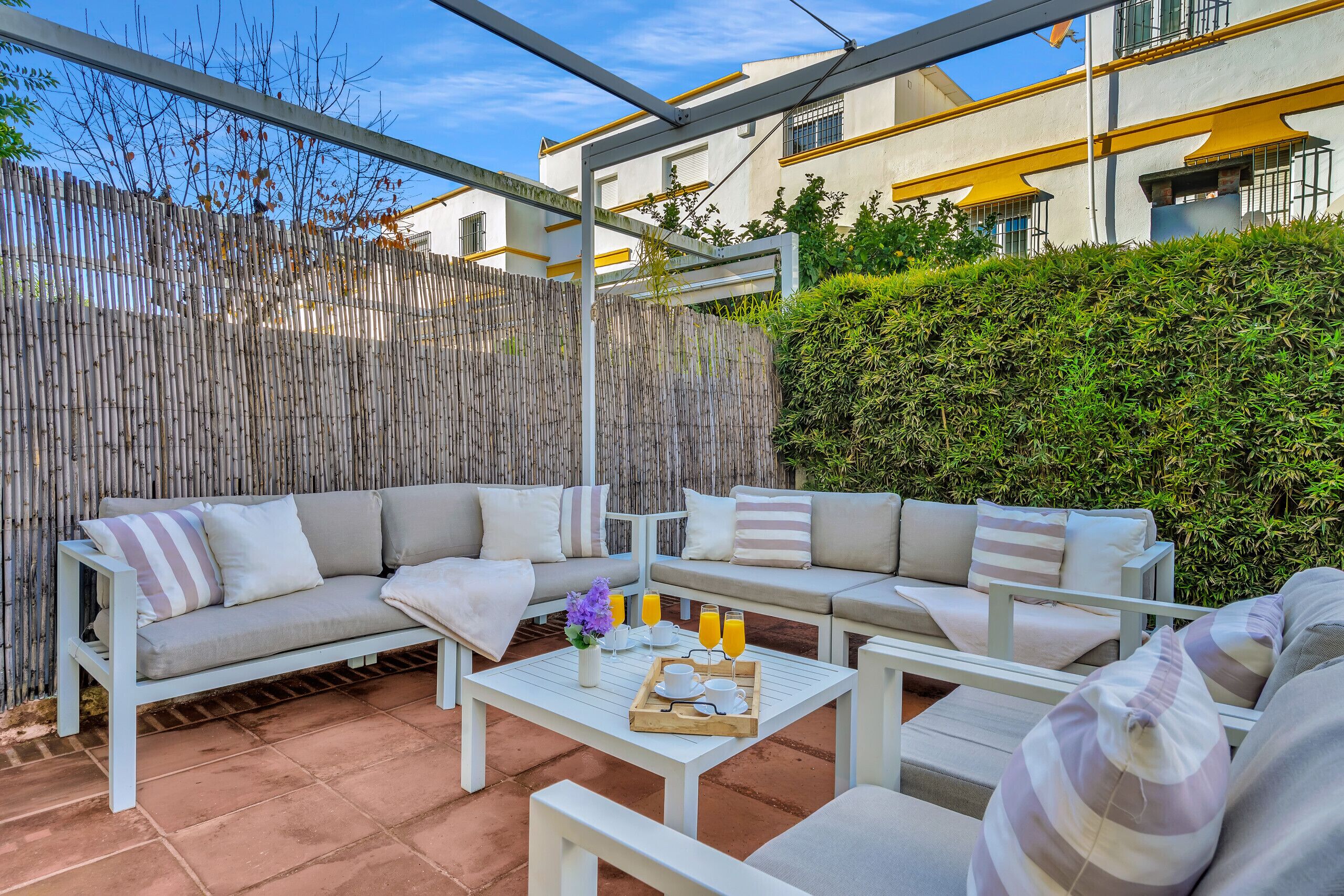 A patio area with a sofa set, a table with a tray of orange juice, and a bamboo fence.