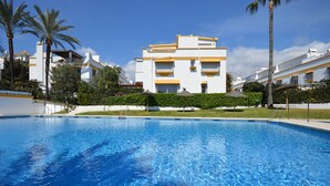 A swimming pool with a clear blue water surface, surrounded by a white building with yellow accents and balconies. - Casa Bella - Marbellamar (Marbella)