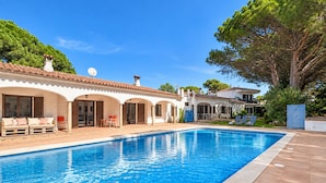 A swimming pool with a tiled edge, a covered patio area with seating, and a building with a tiled roof and arches. - FRANCIAC: Cosy house with a large community pool and garden (l'Escala)