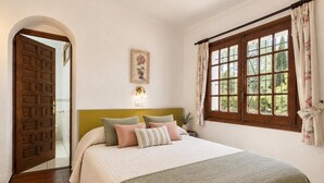 A bedroom with a bed, a headboard, a window with curtains, a door, and a wall-mounted light fixture. - FRANCIAC: Cosy house with a large community pool and garden (l'Escala)