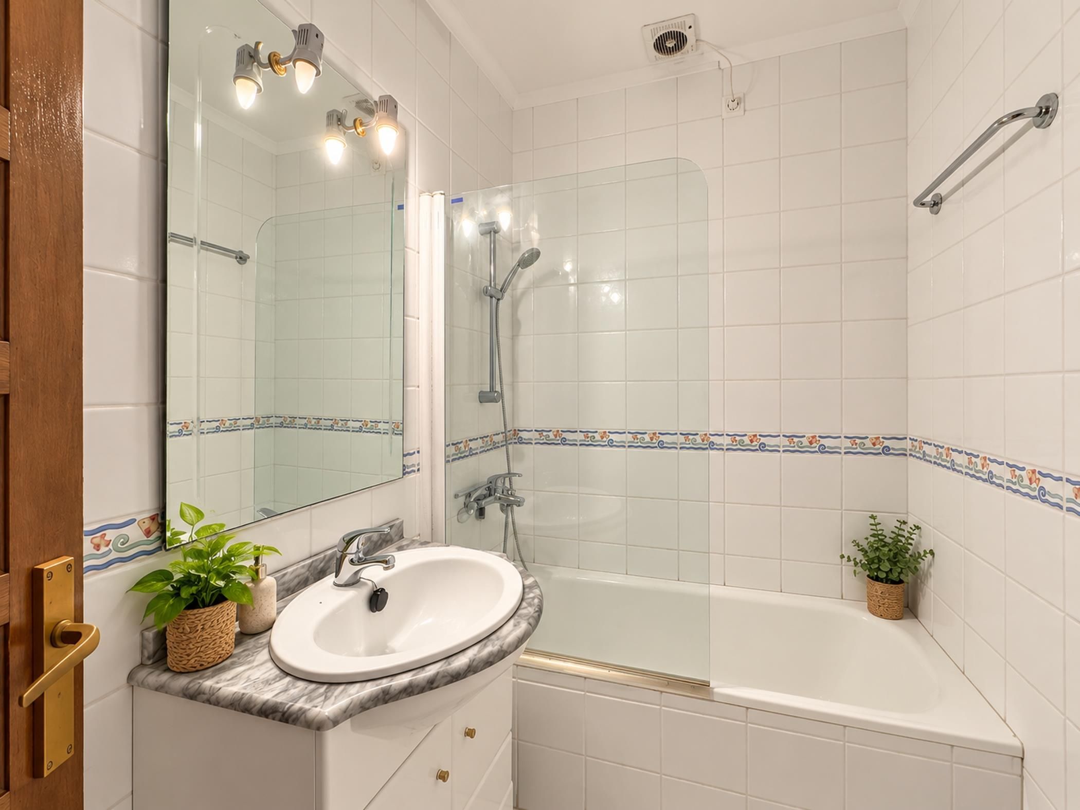 Un baño con lavamanos blanco, espejo, ducha y bañera.