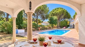 A poolside dining area with a table set for four, surrounded by columns and a view of a swimming pool. - FRANCIAC: Cosy house with a large community pool and garden (l'Escala)