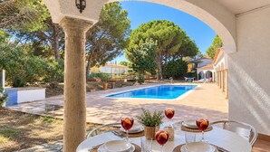 An outdoor dining area with a pool, surrounded by trees and a clear sky. - FRANCIAC: Cosy house with a large community pool and garden (l'Escala)