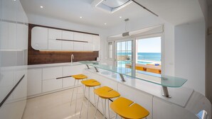 Une cuisine moderne avec un bar en verre et des tabourets jaunes, un mur d’accent en bois et une vue sur la mer.