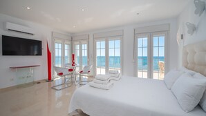 Une chambre spacieuse avec un grand lit, un téléviseur fixé au mur et un balcon offrant une vue sur la mer.