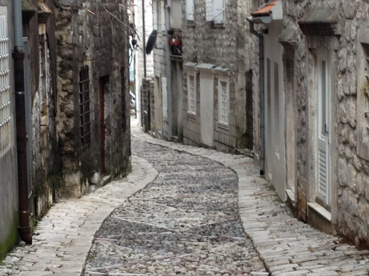 Una estrecha calle adoquinada bordeada por edificios de piedra con ventanas y puertas con rejas.