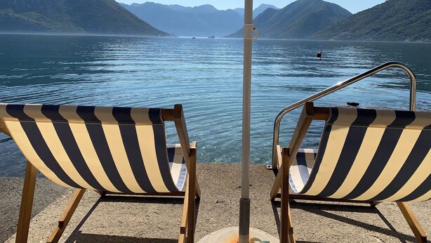 Two striped lounge chairs with an umbrella, overlooking a calm lake with mountains in the background. - A unit, One bedroom, stunning views, waterfront, free secured parking (Lipci)
