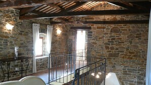 A rustic room with stone walls, a wooden ceiling, a white sofa, a chair, and a staircase with a metal railing. - Romantic-serene villa - heated swimming pool and superb view of the valley (Pengari)