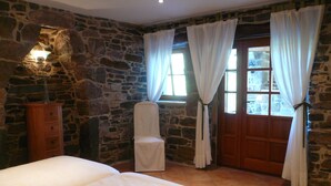 A bedroom with a stone wall, a wooden cabinet, a chair, a bed, and a door with curtains. - Romantic-serene villa - heated swimming pool and superb view of the valley (Pengari)
