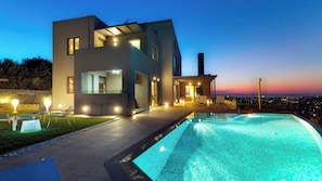 Uma casa moderna com piscina, área de estar externa e vista para a cidade ao entardecer.