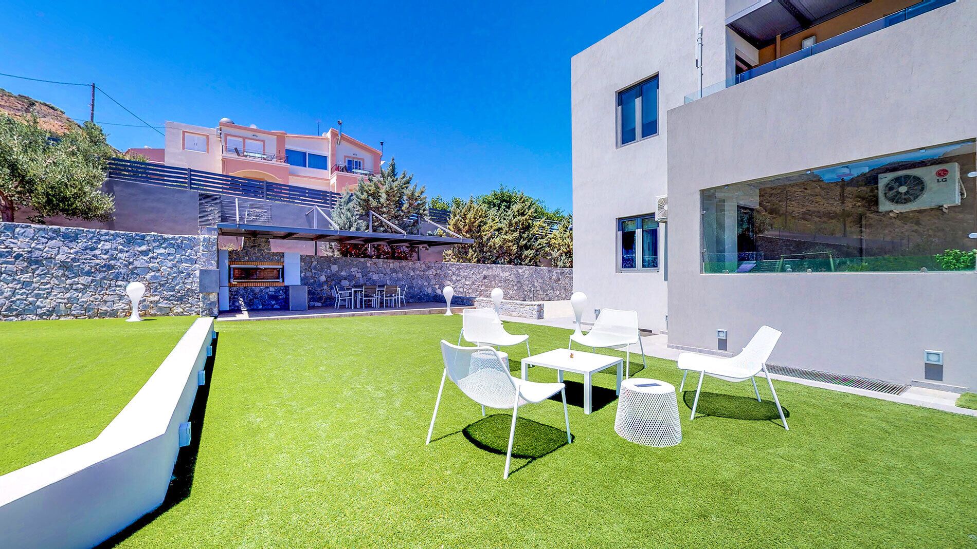 A modern outdoor patio with artificial grass, white chairs, and a stone wall.
