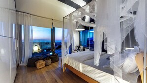 A modern bedroom with a large bed, sheer curtains, and a view of the cityscape.