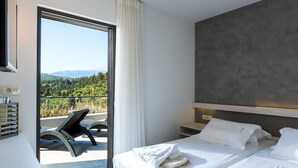 A modern hotel room with a large sliding glass door leading to a balcony with a scenic view of greenery and mountains.