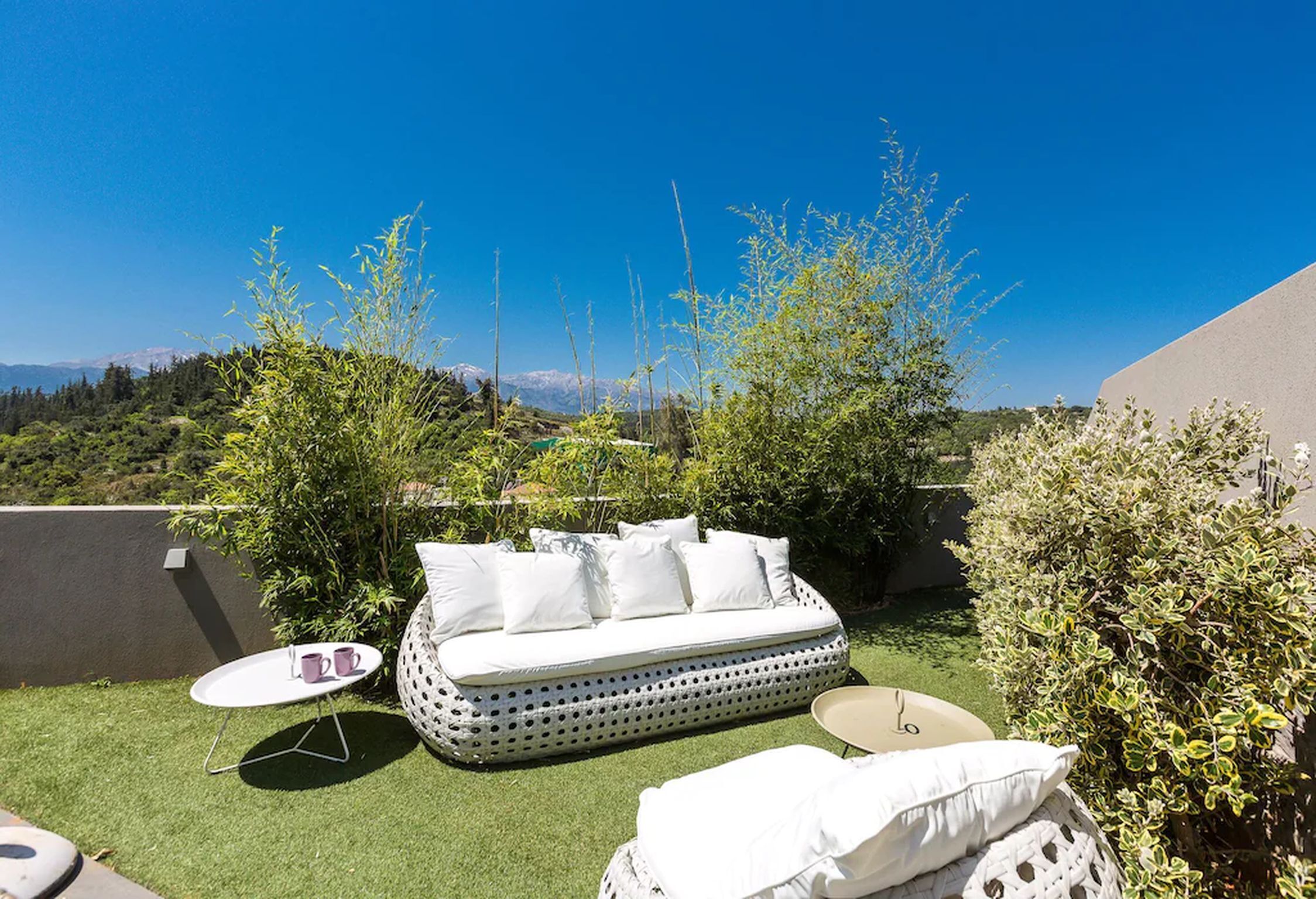 An outdoor seating area with a white sofa, two small round tables, and a view of distant mountains.