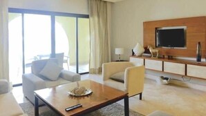 A modern living room with a flat-screen TV mounted on a wooden wall, a ceiling fan, and a large window with curtains. - INCREDIBLE WATER FRONT APARTMENT WITH AMAZING VIEW (CAP CANA)