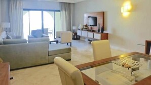 A modern hotel room with a sofa, armchair, dining table, TV, and a large window. - INCREDIBLE WATER FRONT APARTMENT WITH AMAZING VIEW (CAP CANA)