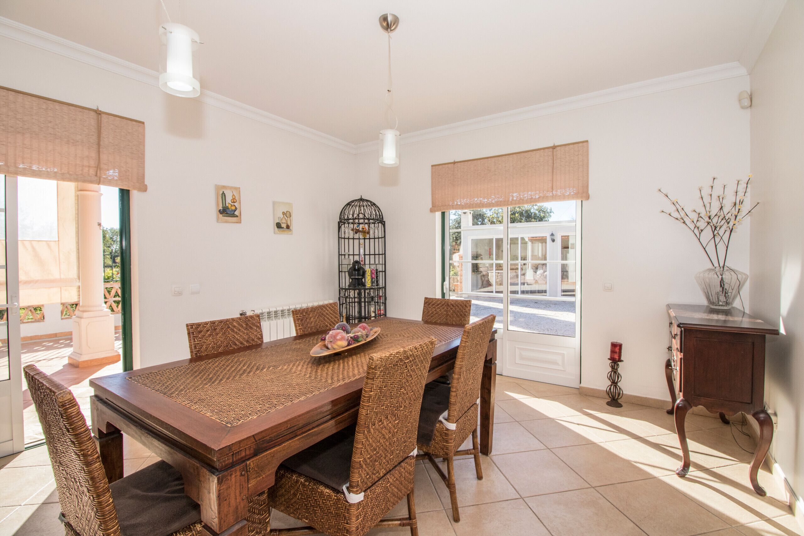 A dining area with a wooden table and wicker chairs, a birdcage, and a vase with branches.