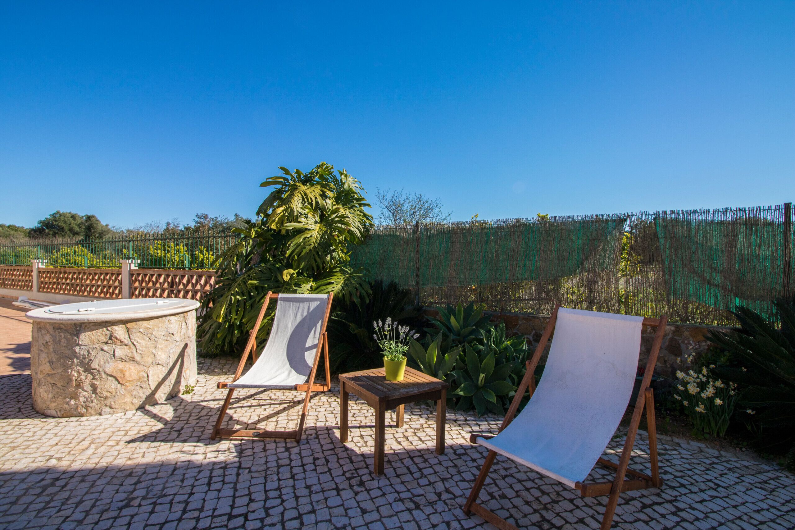 Eine Terrasse im Freien mit zwei Liegestühlen, einem kleinen Tisch mit einem Topfpflanzen und einem Steintisch.