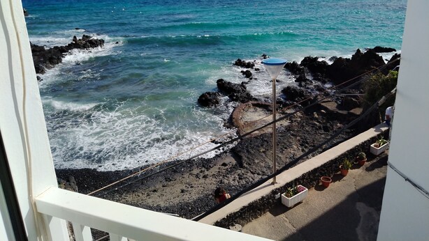 A balcony with a view of the ocean, rocky shoreline, and potted plants. - Traditional seafront ground floor apartment. Children free in summer. (Punta Mujeres)