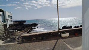 A coastal view with a street lamp, rocky shoreline, and a building with a white facade. - Traditional seafront ground floor apartment. Children free in summer. (Punta Mujeres)