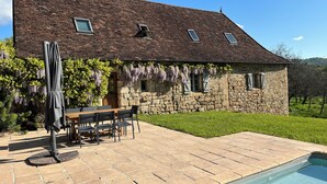 Ein Steinhaus mit einer gefliesten Terrasse, einem Pool und einer Essgegend.