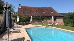 Ein Steinhaus mit Swimmingpool, Gartenmöbeln und Sonnenschirmen.