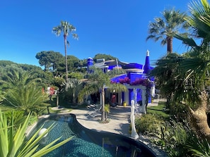 A pool surrounded by tropical plants and a blue building with a white roof. - Large luxury detached villa 4 en-suite bedrooms private pool golf at 300 meters (VILAMOURA)