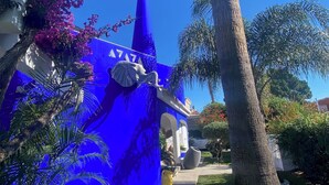 A blue building with a white dome, surrounded by palm trees and purple flowers.