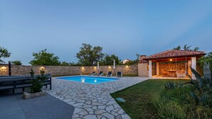 Un patio trasero con una piscina de piedra, sillones de descanso y un área de patio con mesa y sillas.