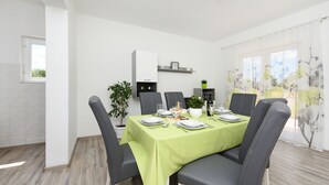 Un comedor con una mesa dispuesta para cuatro personas, sillas, una planta en maceta y una estantería con objetos decorativos.