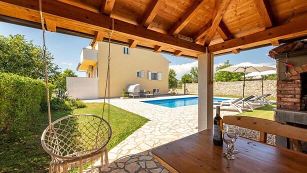Una pérgola de madera con un columpio colgante, una piscina y una zona de barbacoa.