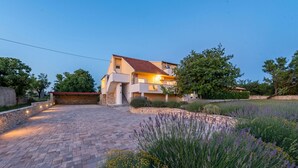 Una casa de dos pisos con entrada pavimentada y un muro de piedra.