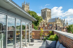 Une terrasse sur le toit offrant une vue sur une cathédrale historique, aménagée avec des meubles d’extérieur et des plantes en pot.