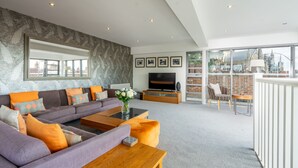 A modern living room with a large sofa, a coffee table, and a TV. There is a balcony with a view of buildings. - 11 Stonegate Court -  a family break that sleeps 4 guests  in 2 bedrooms (York)