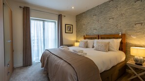 A neatly made bed with a headboard, a bedside lamp, and a window with curtains. - 11 Stonegate Court -  a family break that sleeps 4 guests  in 2 bedrooms (York)
