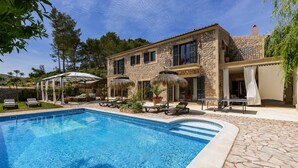 Une maison en pierre avec une piscine, un espace salon extérieur et une terrasse couverte.