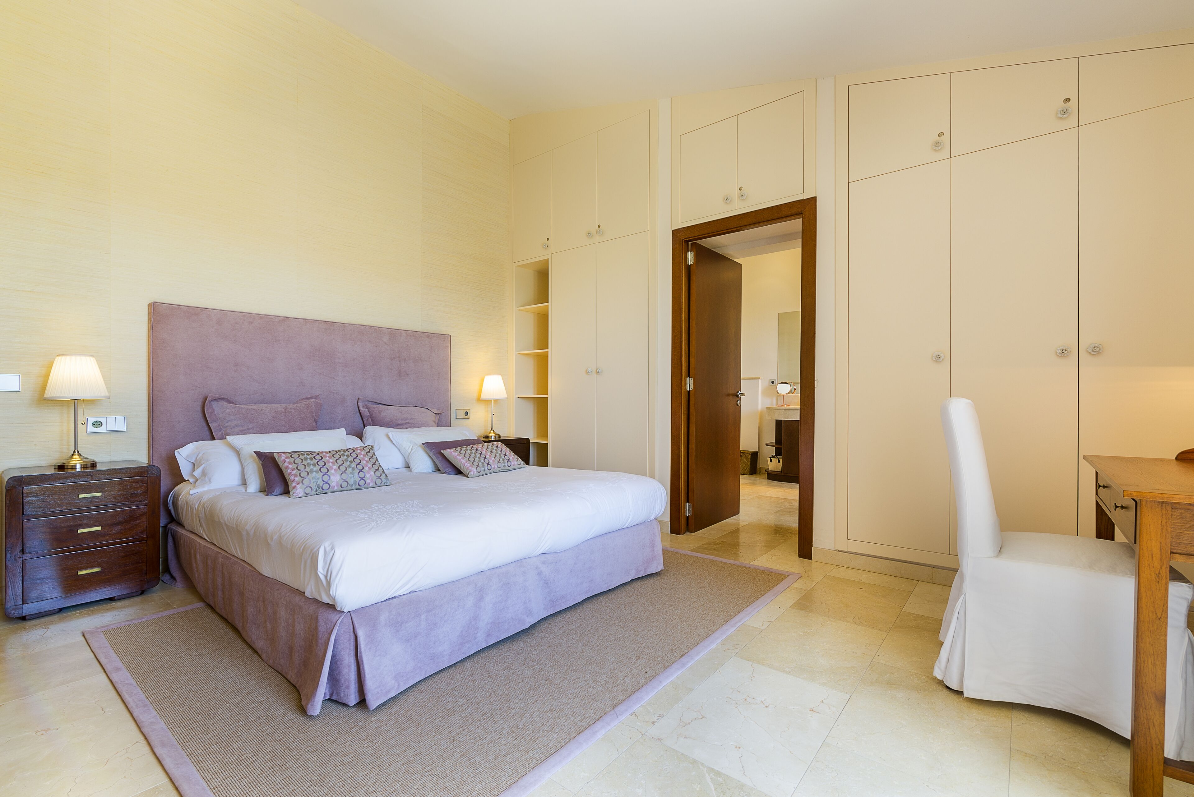 A neatly arranged bedroom with a bed, bedside tables, a chair, and a wardrobe.