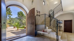 Un intérieur spacieux donnant sur un espace extérieur aménagé, une porte en bois, un escalier avec une rampe en métal et un banc où est assis un chien.