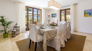 Un coin repas avec une table dressée pour quatre personnes, de grandes fenêtres et une plante en pot.
