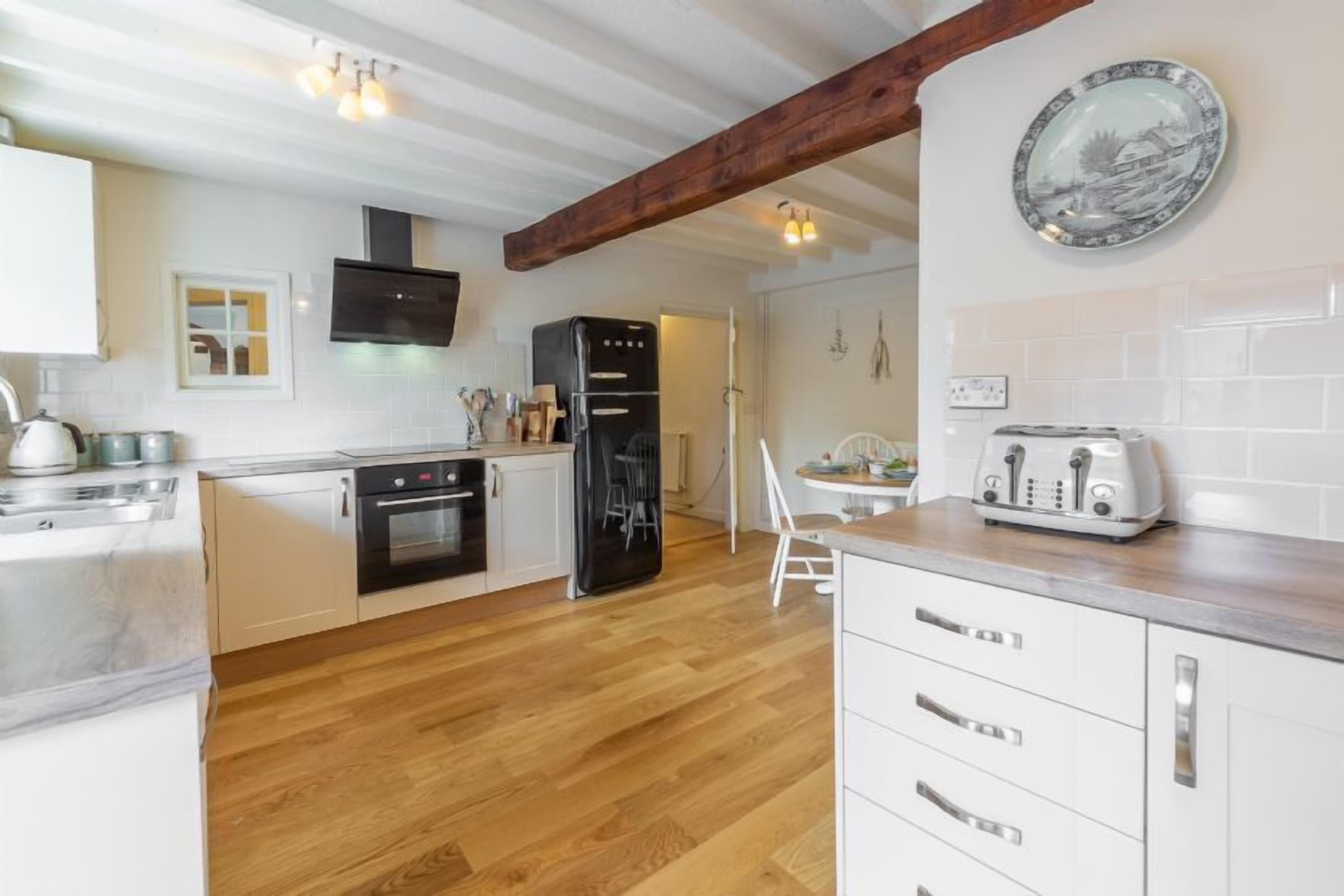 A modern kitchen with white cabinetry, a black refrigerator, and a wooden floor.