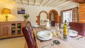 Un coin repas avec une table en bois dressée pour deux personnes, un buffet avec des portes en verre et un mur de briques agrémenté d’une fenêtre en arc de cercle.