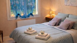 Ein Schlafzimmer mit einem großen Bett, einem Fenster mit blauen Vorhängen, einem Nachttisch mit einer Lampe und einem Gemälde an der Wand.