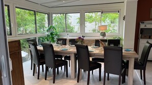 Ein Essbereich mit einem großen Tisch, gedeckt für sechs Personen, umgeben von schwarzen Stühlen und Blick auf Grünanlagen durch große Fenster.