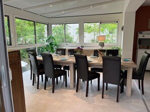 A dining area with a large table set for six, surrounded by black chairs, with a view of greenery outside through large windows. - Big House 10/ 13 persons ***3 keys 150 meters from the beach (La Tranche-Sur-Mer)