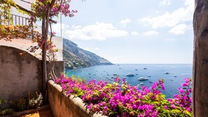 A balcony with vibrant pink flowers and a view of the sea with boats.
