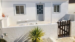A white building with a red-tiled roof, a white door, and windows. There is a white chair outside and a potted plant in the foreground. - Salty Soul Beach House (Costa da Caparica)