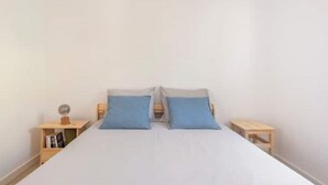 A simple, clean room with a bed, two pillows, and two bedside tables with a globe and books. - Salty Soul Beach House (Costa da Caparica)