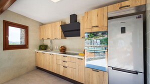 Eine moderne Küche mit Holzausstattung, einem Edelstahlkühlschrank und einem Fenster mit Blick auf einen Pool.