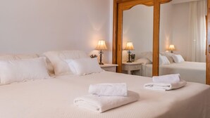 Ein Hotelzimmer mit einem großen Bett, zwei Nachttischen mit Lampen, einem Spiegel und einem Fenster mit Vorhängen.