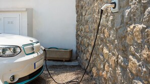 Ein weißes Auto, verbunden mit einer Ladestation für Elektrofahrzeuge, die an einer Steinmauer befestigt ist.